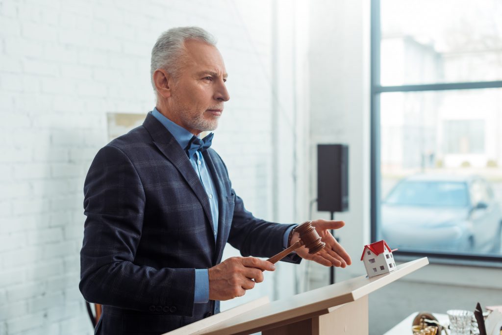 auctioneer pointing with hand at model of house and holding gavel during auction