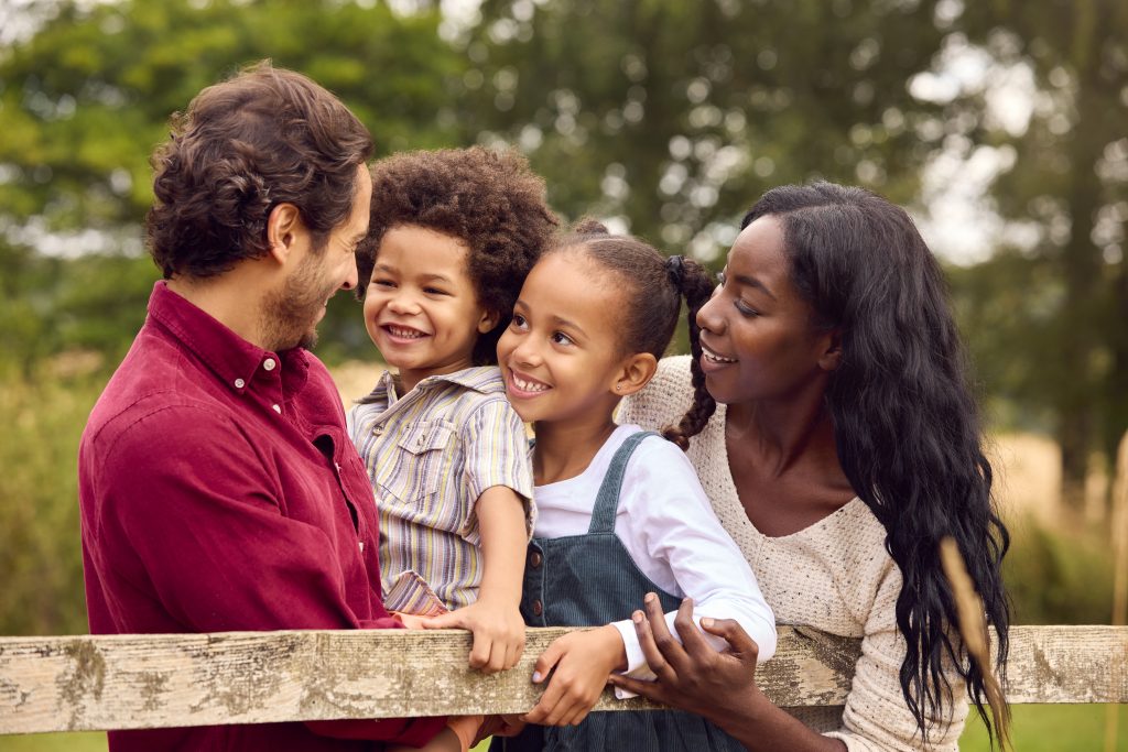 Loving Mixed Race Family Leaning On Fence On Walk In Countryside