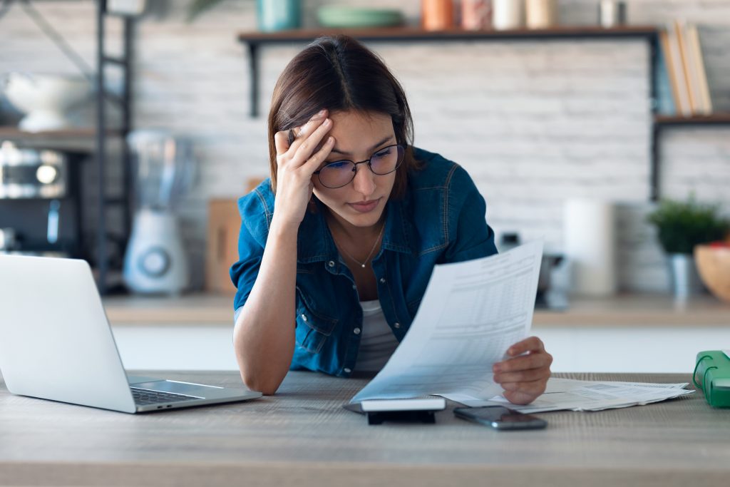 young woman working with computer while consulting some invoices and documents in the kitchen